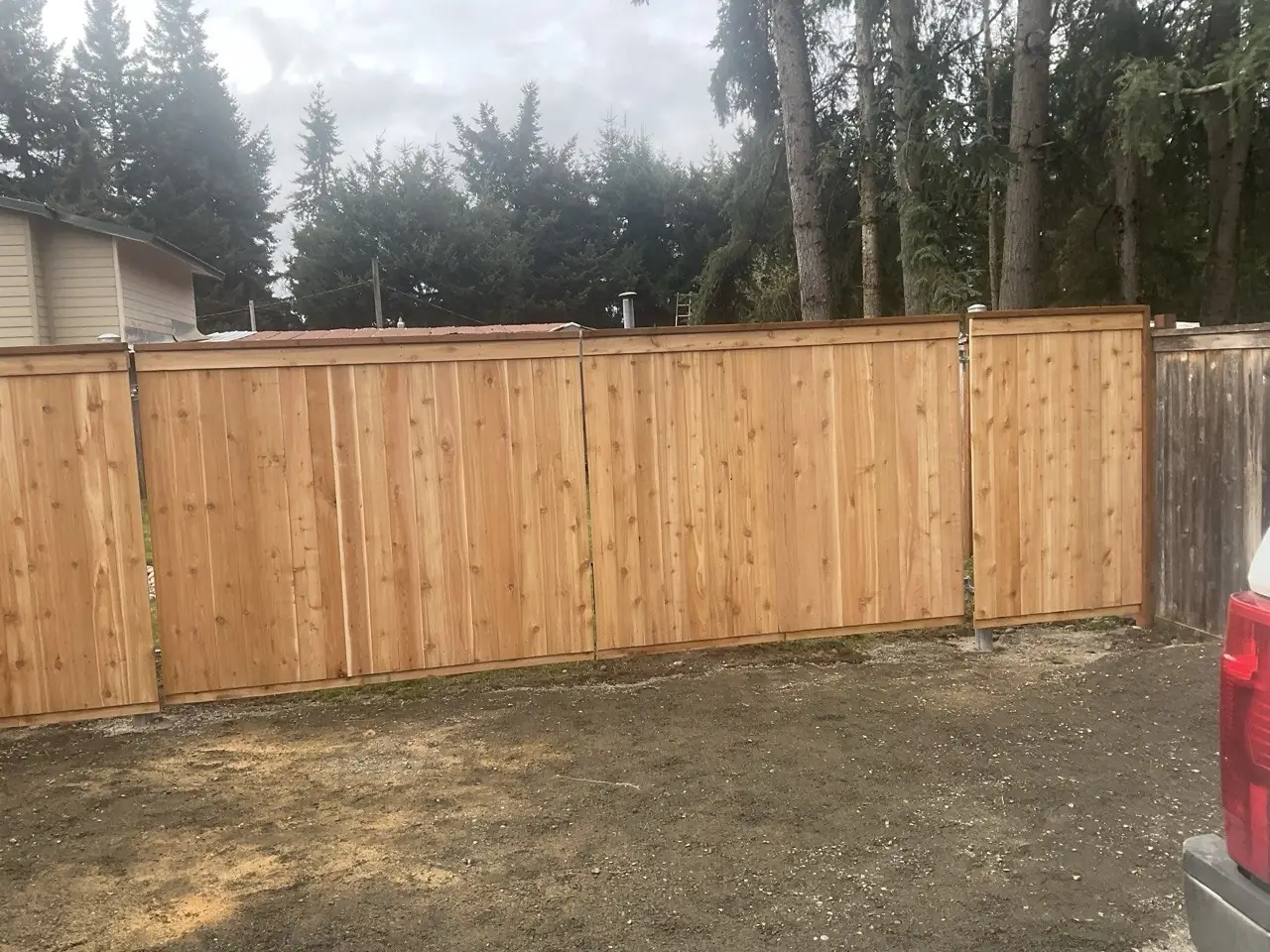 Capped cedar privacy fence running along a residential driveway in Western Washington
